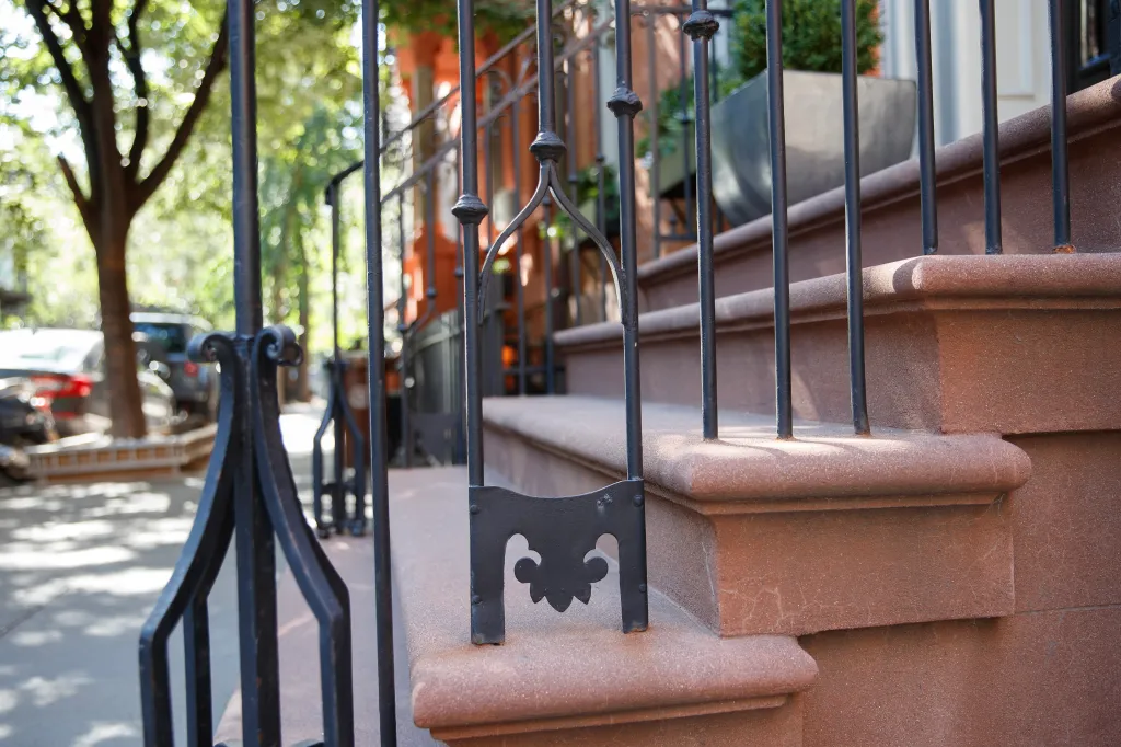 A metal bootscraper attached to a railing on a brownstone stoop in New York City.