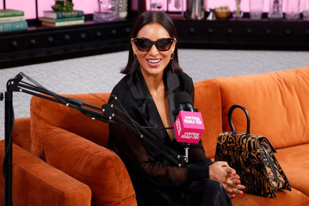 Jessel Taank smiling in sunglasses, sitting on an orange couch next to a microphone with
