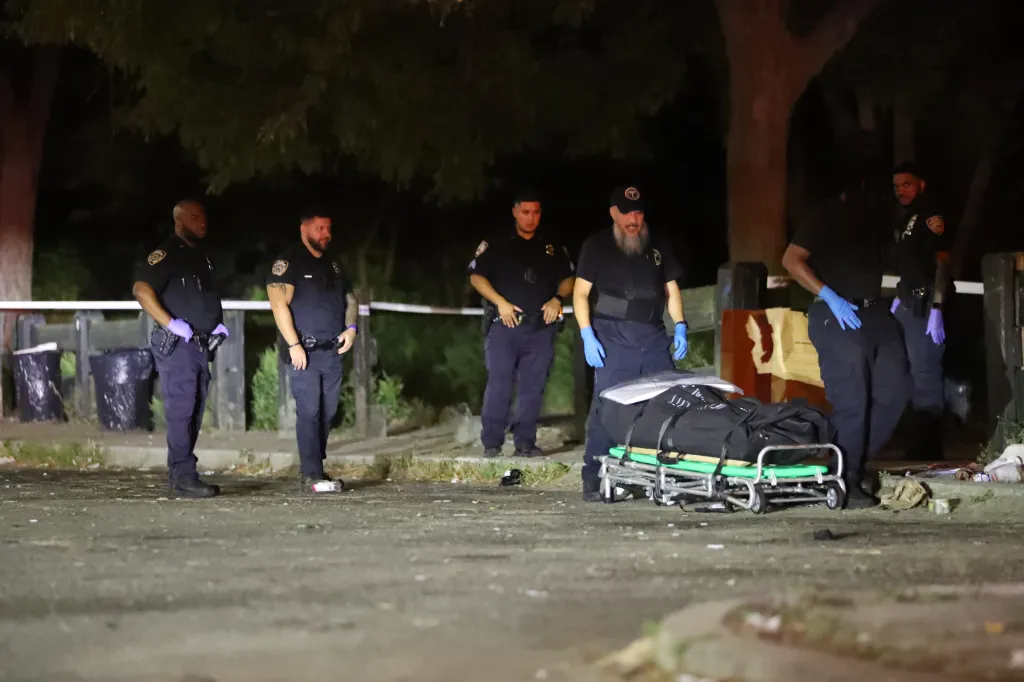 Police officers and medical examiners at a death investigation scene, with a body on a stretcher.