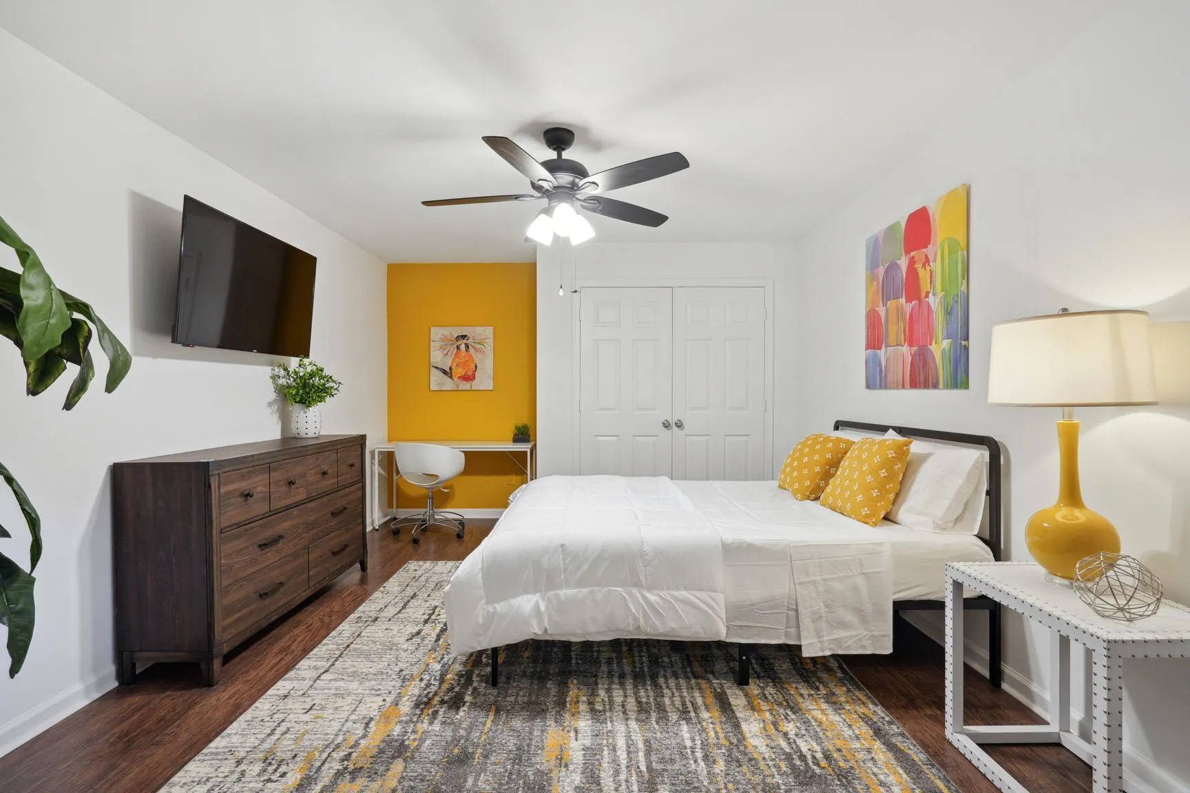A small bedroom with queen bed, ceiling fan, and a TV hanging above a dresser. A small bedroom with queen bed, ceiling fan, and a TV hanging above a dresser.