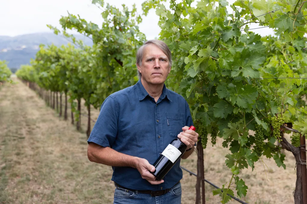 Jim Lincoln in a vineyard, holding a bottle of wine.