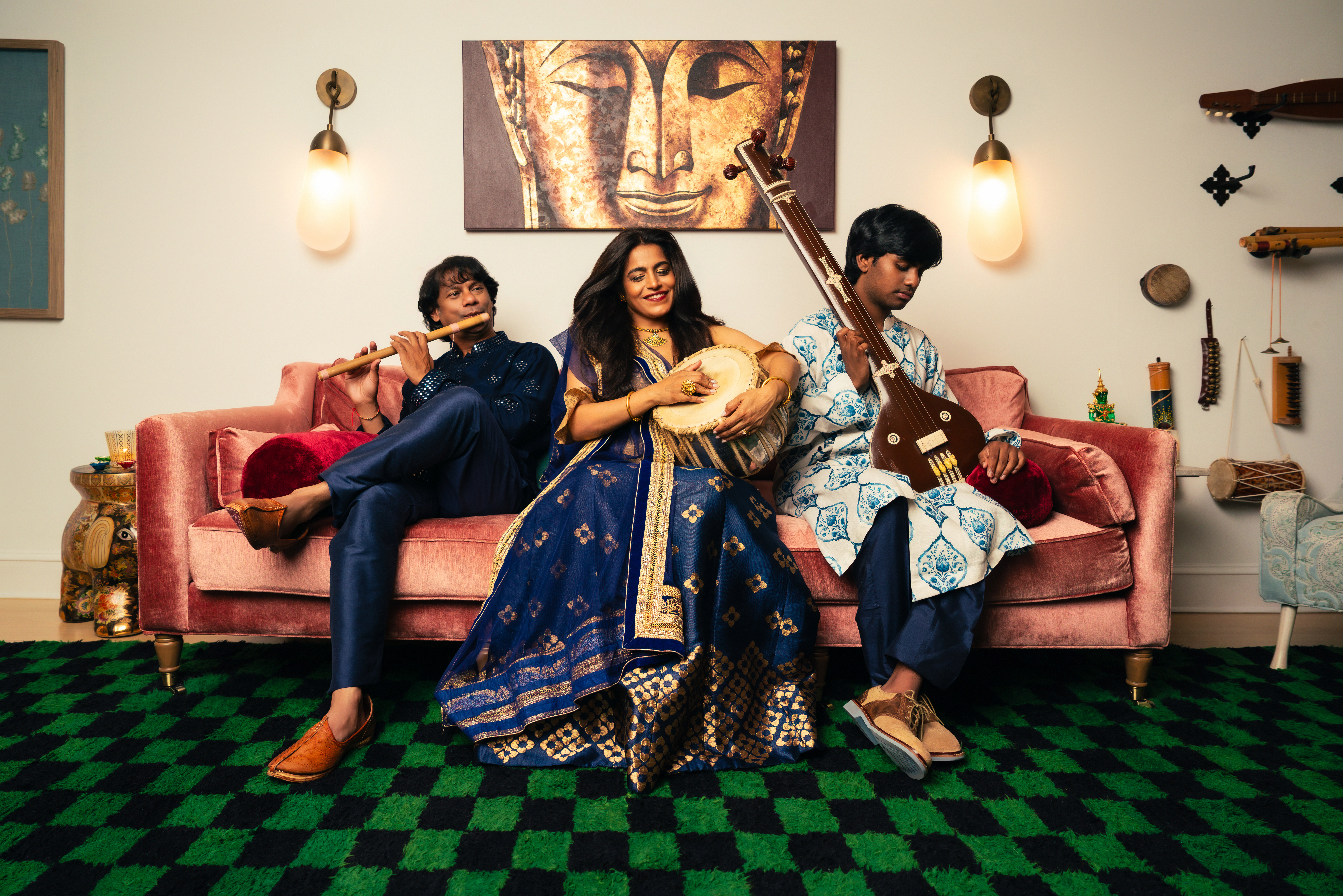 Falu with her husband and son sitting on a pink couch, each holding a traditional Indian musical instrument.