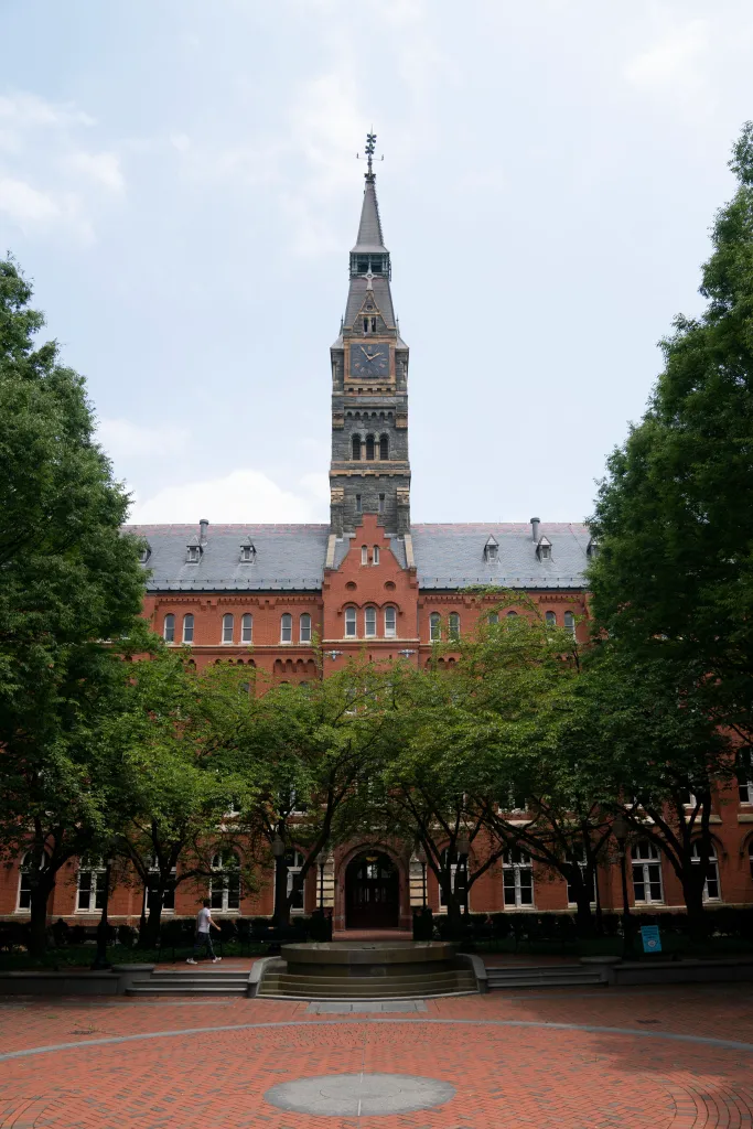 Georgetown University's Healy Hall with its clock tower, seen from a brick courtyard partially obscured by trees.