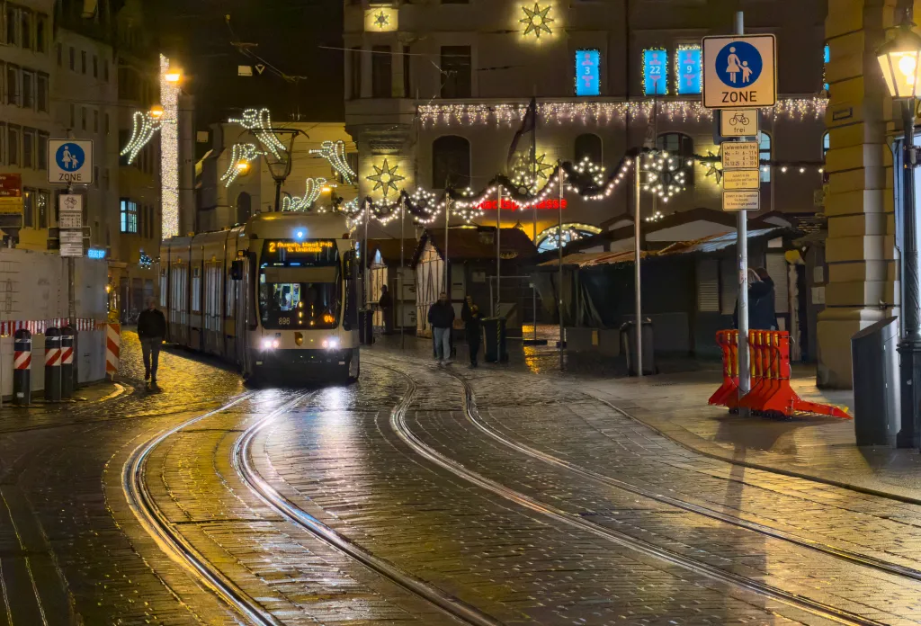  Vibrant night scene of a city street lit by angel-wing Christmas lights, tram cars gliding on wet tracks, and vivid reflections creating a festive urban mood on November 30, 2025 in Augsburg, Germany.