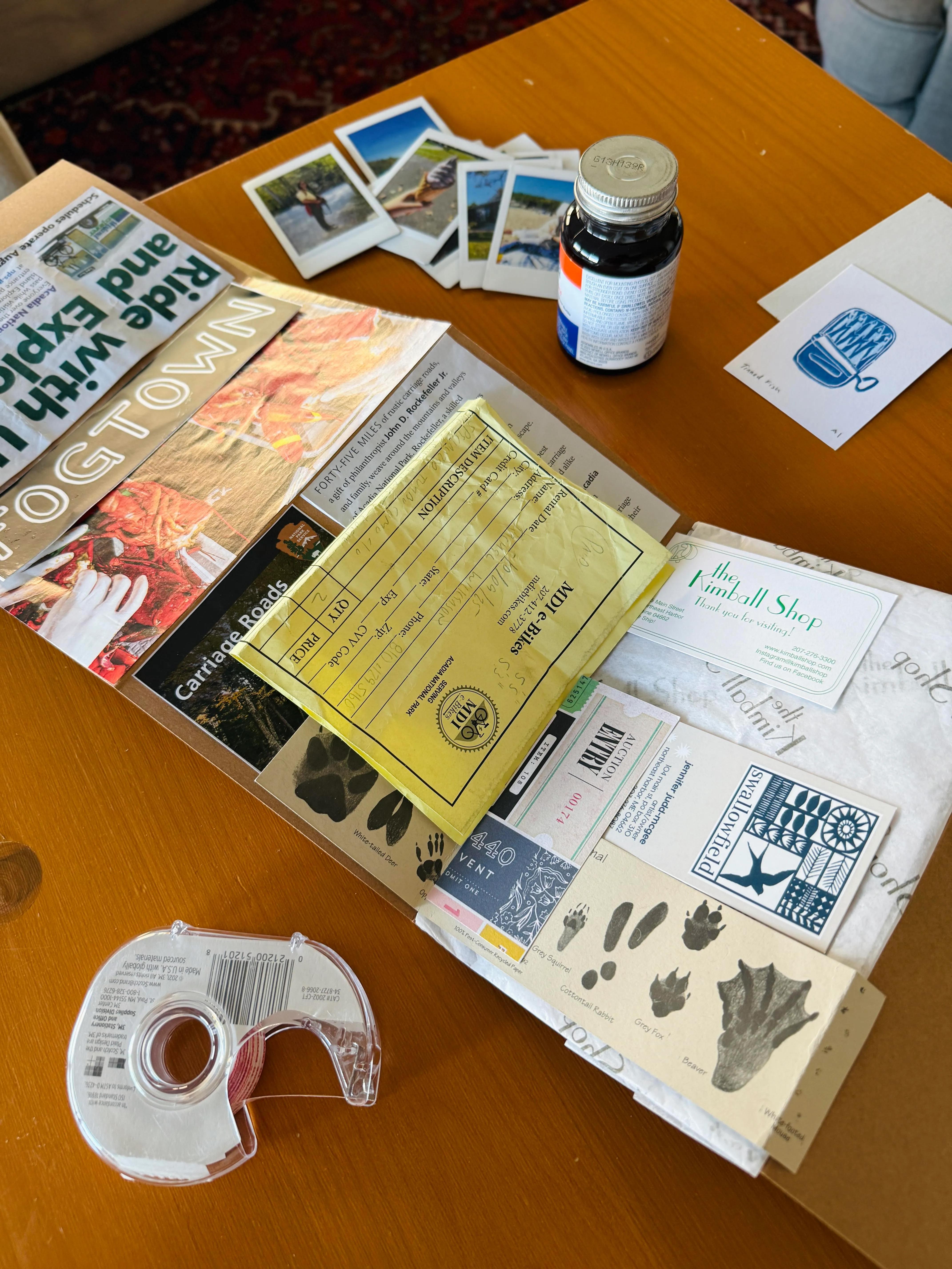 a photo of a travel junk journal in progress, with scraps, receipts, and souvenirs. There is tape, rubber cement, and Instax photos on the table next to the journal