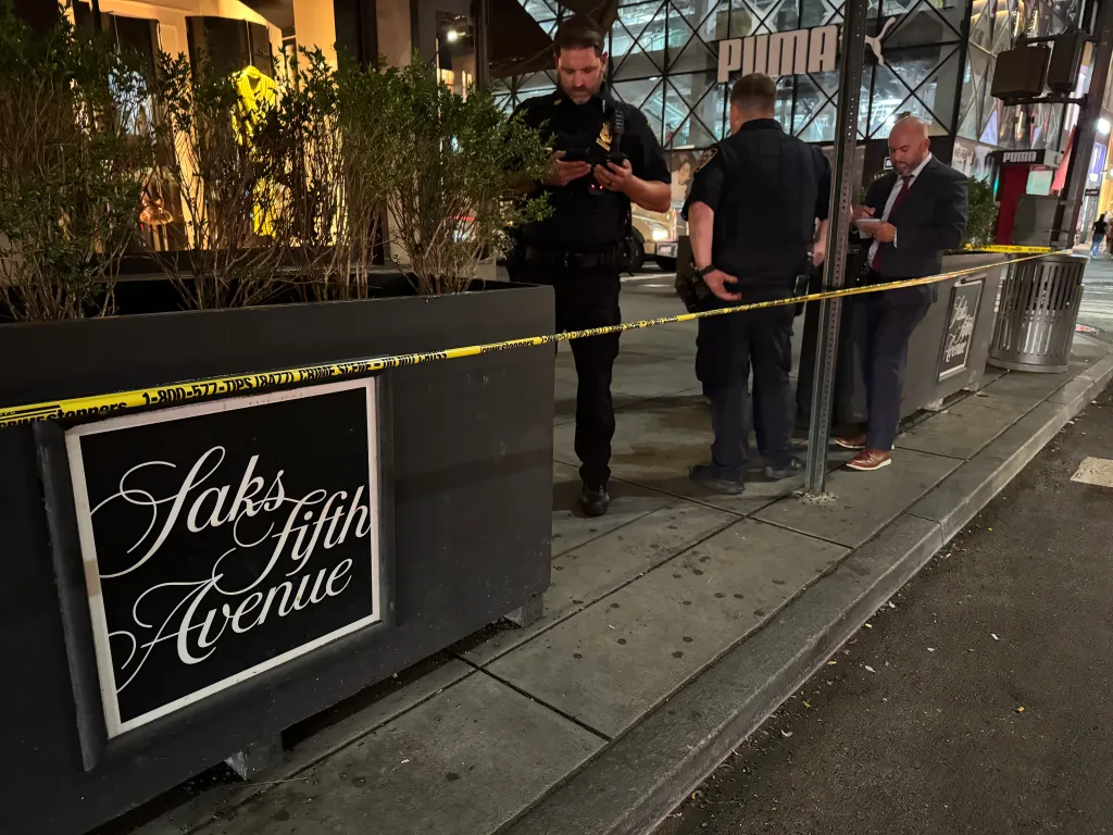Crime scene tape in front of a Saks Fifth Avenue sign with police officers.