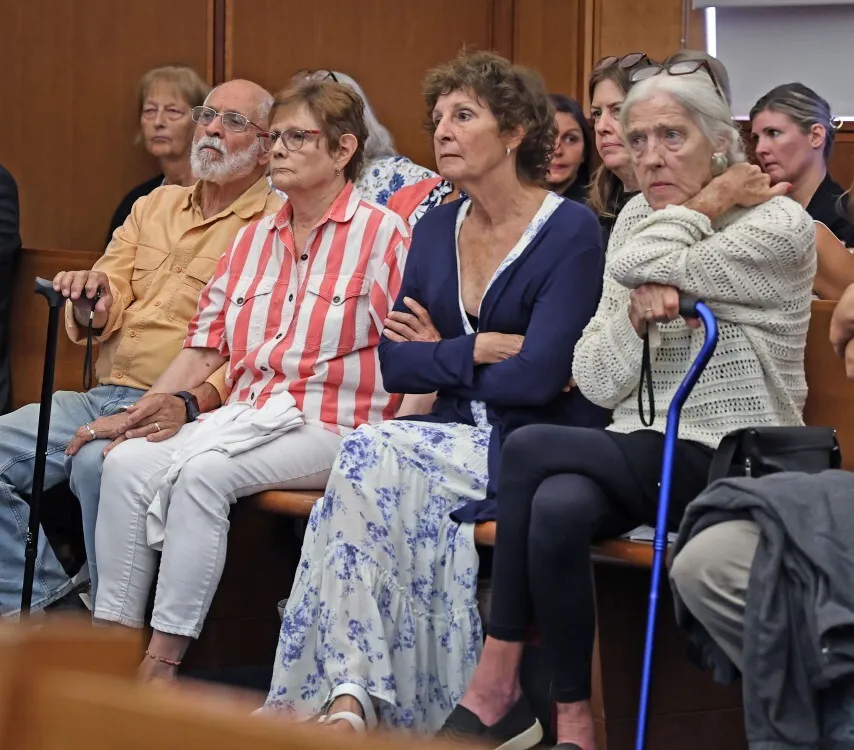 Several older adults sitting on wooden benches in a courtroom, listening intently.