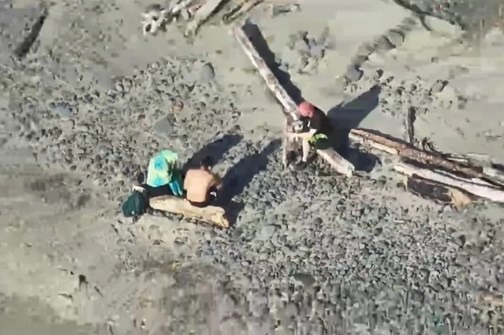 People on an Oregon beach sit next to driftwood logs.