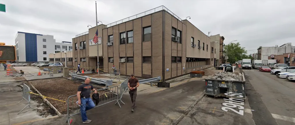A brown brick building with an American flag and construction barriers around it, with 