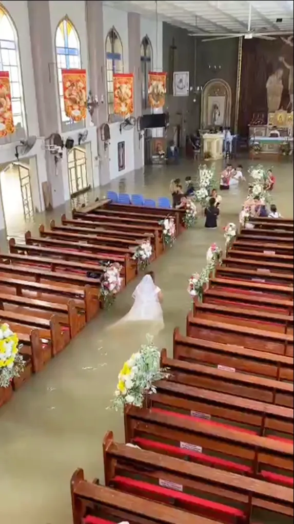 A bride walks down a flooded church aisle towards guests standing in water.