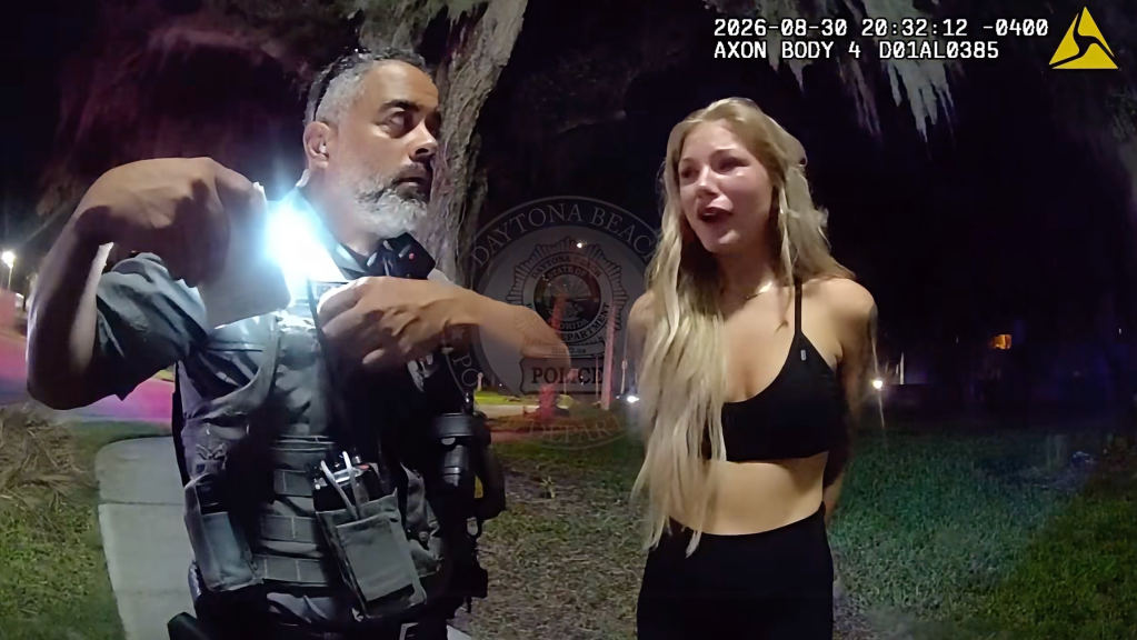 A police officer shining a flashlight on a woman at night.