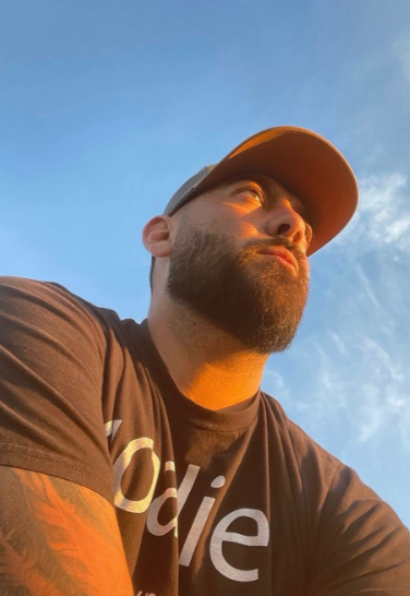 A man with a beard and baseball cap looking up at the sky.