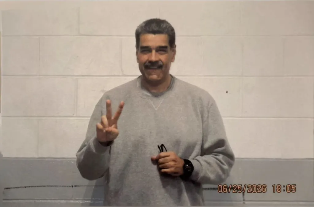 A man in a grey sweatshirt making a peace sign with his left hand.