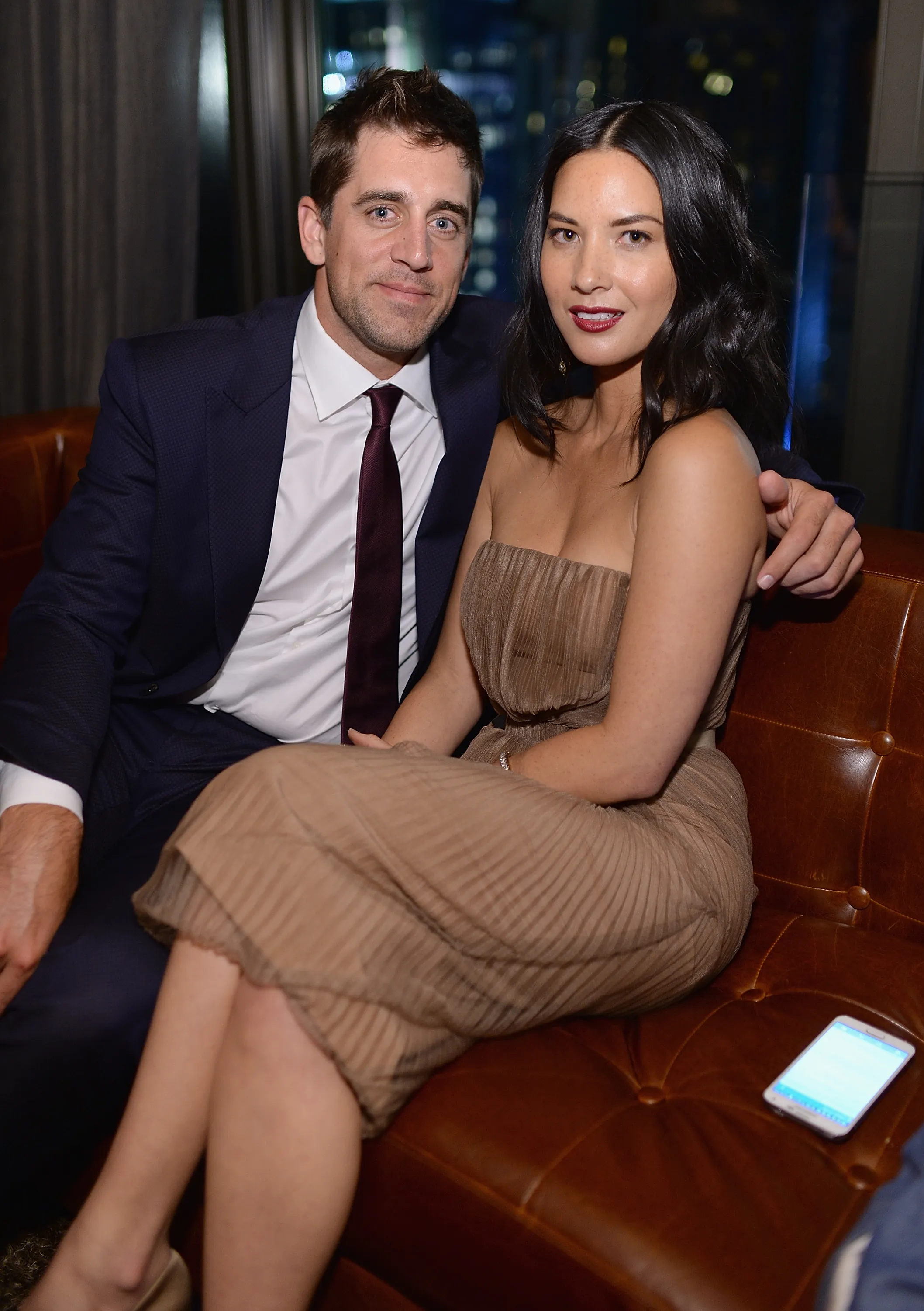 Aaron Rodgers and Olivia Munn sitting on a brown leather couch.