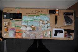 A table covered with bags of drugs, money, guns, and drug paraphernalia.