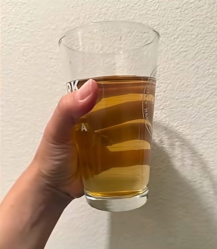 A hand holds a glass of brown, cloudy tap water.