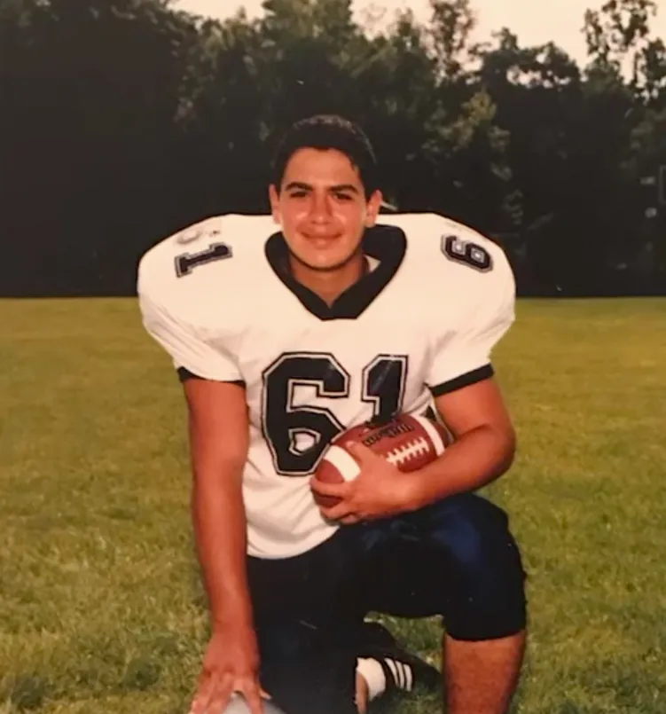 Abdul El-Sayed on his high school football team, kneeling and holding a football.