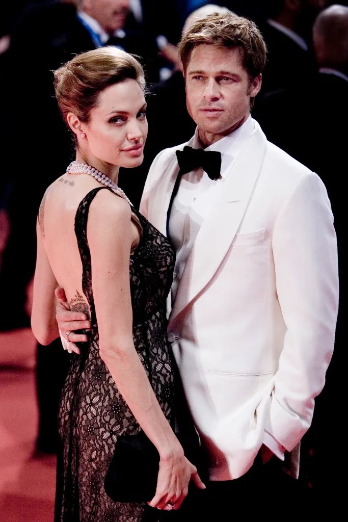 Angelina Jolie in a black lace dress and Brad Pitt in a white tuxedo, with his arm around her waist, at the Venice Film Festival.