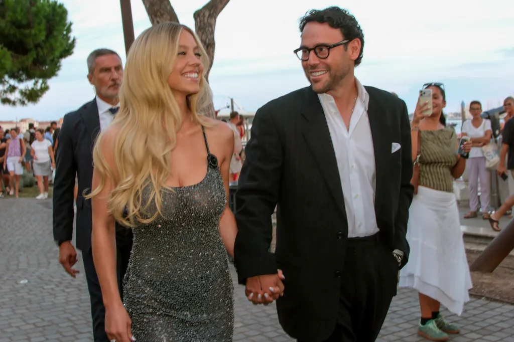 Sydney Sweeney, in a sheer black gown, and Scooter Brown , in a black suit and white shirt, arrive hand in hand at the Armani Beauty party in Venice.