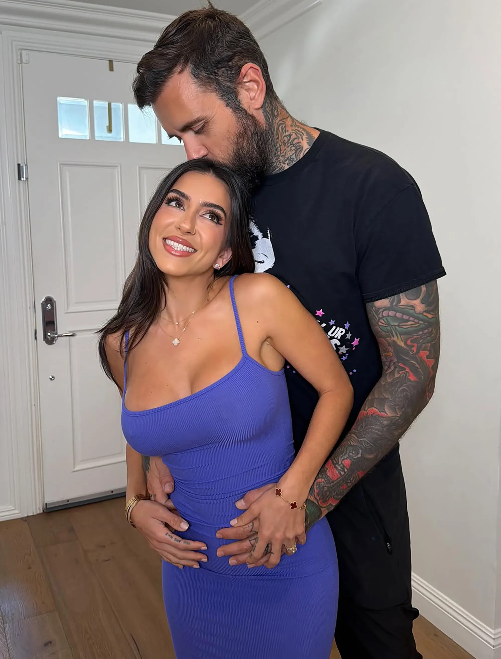 A man with tattoos kissing a woman's forehead, both smiling.