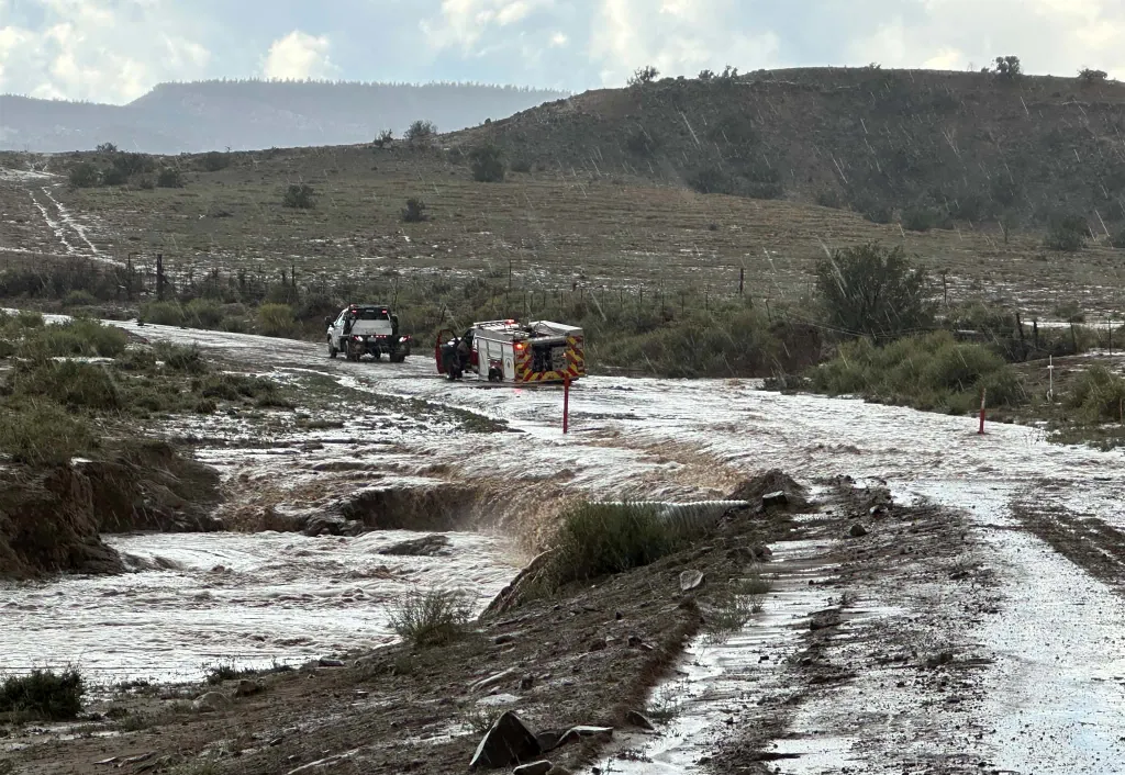 Emergency vehicles on a muddy road next to a flooded, muddy river in Mexican Springs, New Mexico.