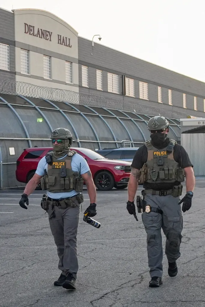 Two Immigration and Customs Enforcement (ICE) agents walk in front of Delaney Hall detention center.