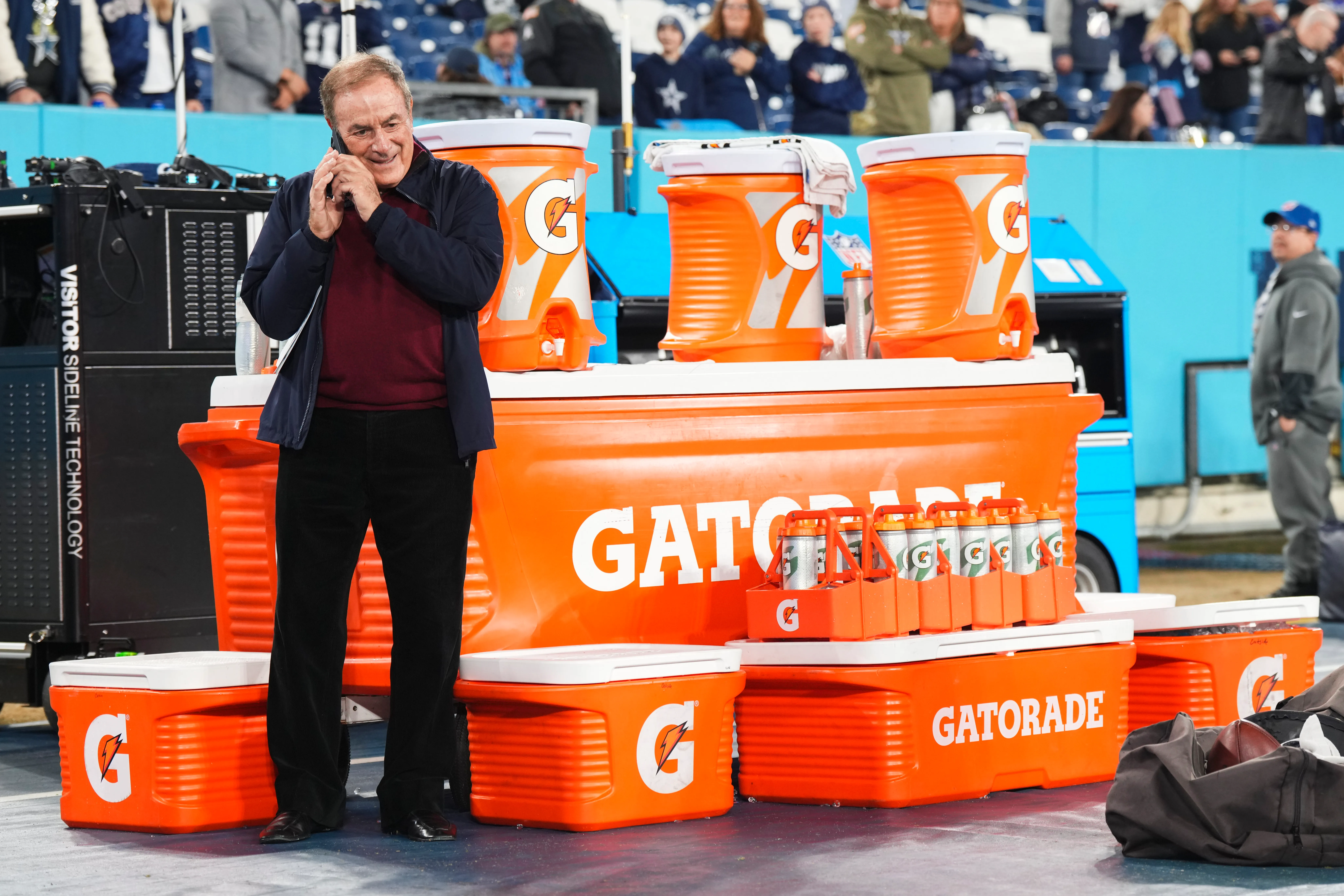 Al Michaels takes a phone call on the Dallas Cowboys bench near Gatorade coolers.