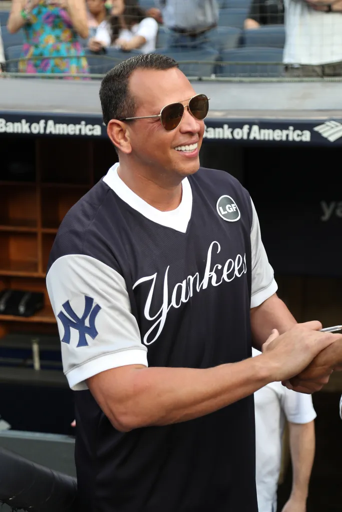 Alex Rodriguez smiling and signing an autograph while wearing a Yankees jersey and sunglasses.