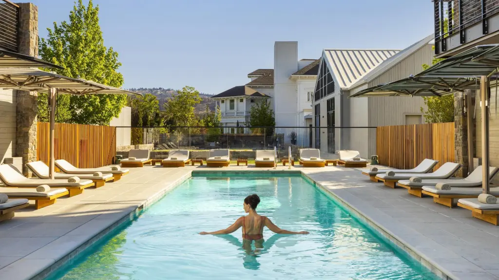 A woman in a red swimsuit stands in the Alila Napa Valley Vineyard View Pool surrounded by lounge chairs and hotel buildings.