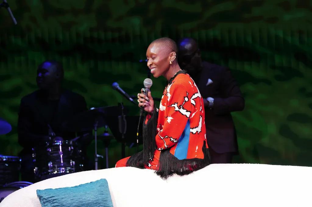 Cynthia Erivo smiling and holding a microphone while sitting at the 