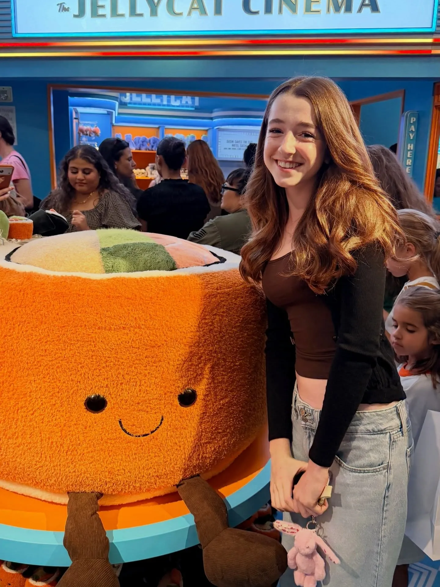 Alyson Hannigan's daughter Keeva smiling next to a large, orange plush toy with a smiling face, in front of 