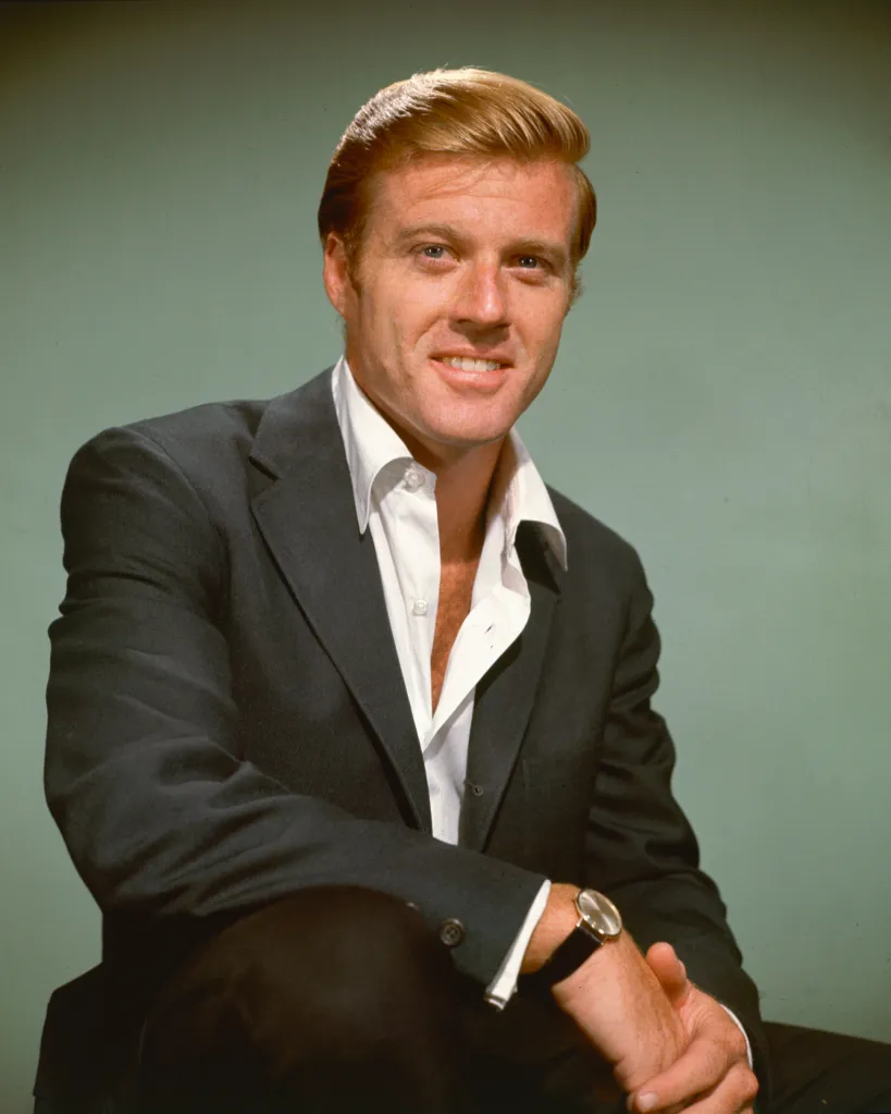 Robert Redford posing for a portrait, wearing a suit jacket and white unbuttoned shirt.