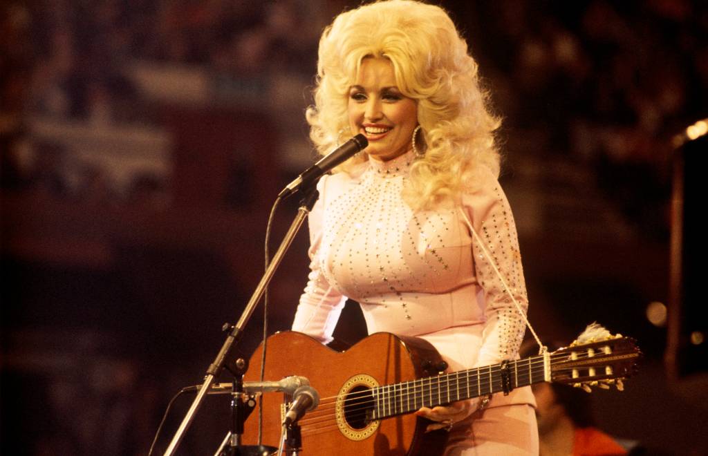 Dolly Parton performing with a guitar and microphone.