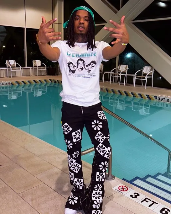 DeShundre Vinson wearing a white t-shirt and patterned black pants, standing by a pool.