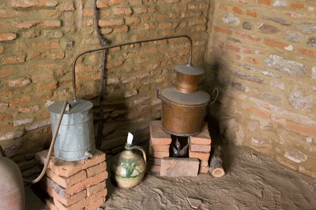 An ancient distiller, made of copper and tin, used for making alcohol, sits in a brick corner.
