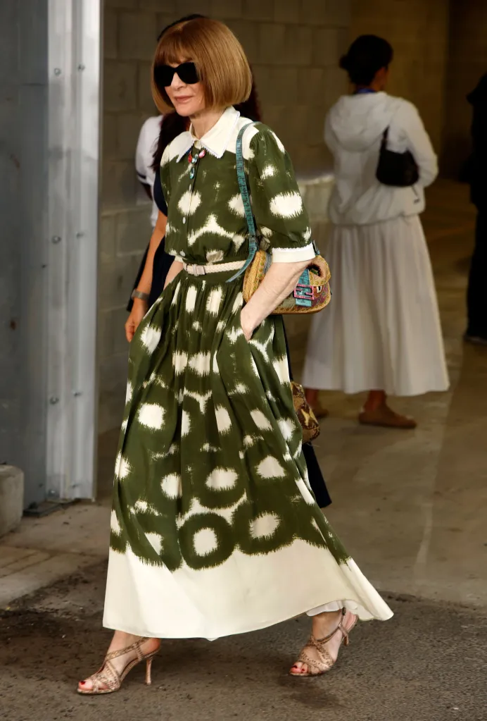 Anna Wintour walking on a blue carpet in a green and white patterned dress.
