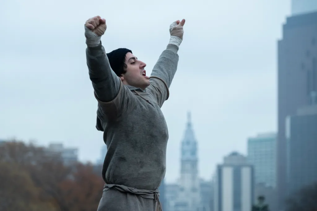 Anthony Ippolito as Sylvester Stallone with arms raised in victory.