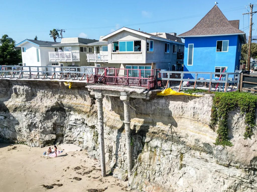 Apartments in Isla Vista, California, are on the edge of a collapsing cliff, with concrete pillars extending to the sandy beach below.