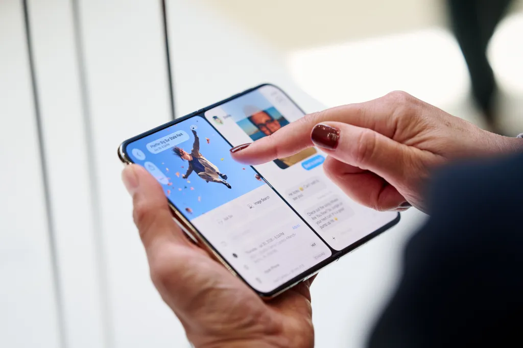 A person's hands holding an unfolded Apple iPhone Duo, displaying an image on the left screen and messages on the right.