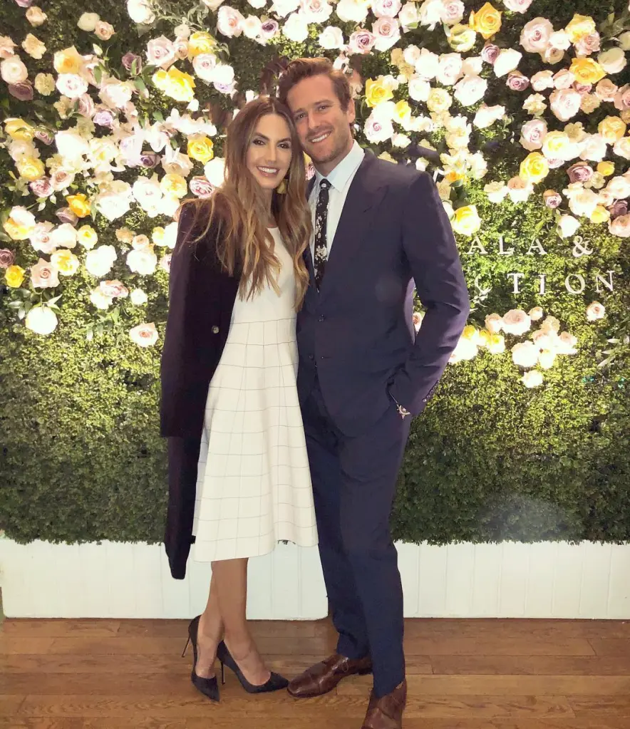 Armie Hammer and Elizabeth Chambers standing together against a flower wall.