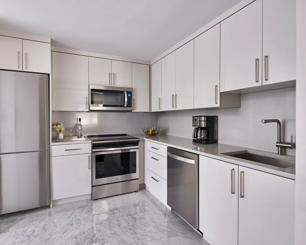 A modern kitchen with white cabinets, stainless steel appliances, and a marble tiled floor.