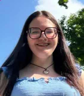 Autumn Setola, a young woman with long dark hair and glasses, smiles at the camera.