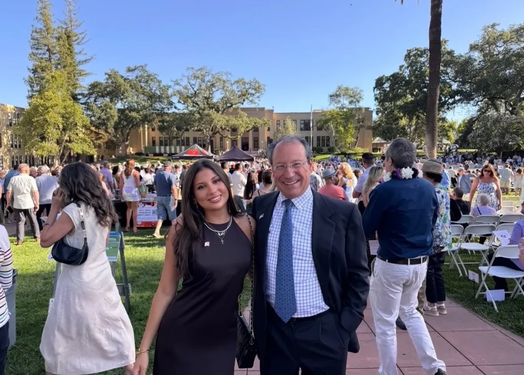 USC senior Ava Schmidt with a man in a suit, standing on a grassy area with a crowd in the background.