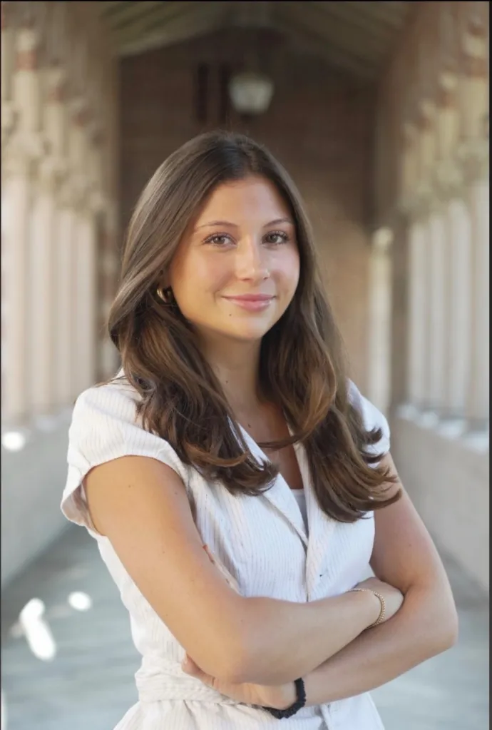 Ava Schmidt, a USC senior, smiles with her arms crossed in front of a building with columns.