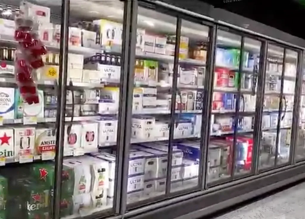 A row of glass-fronted refrigerators in a store, filled with various brands and packs of beer.