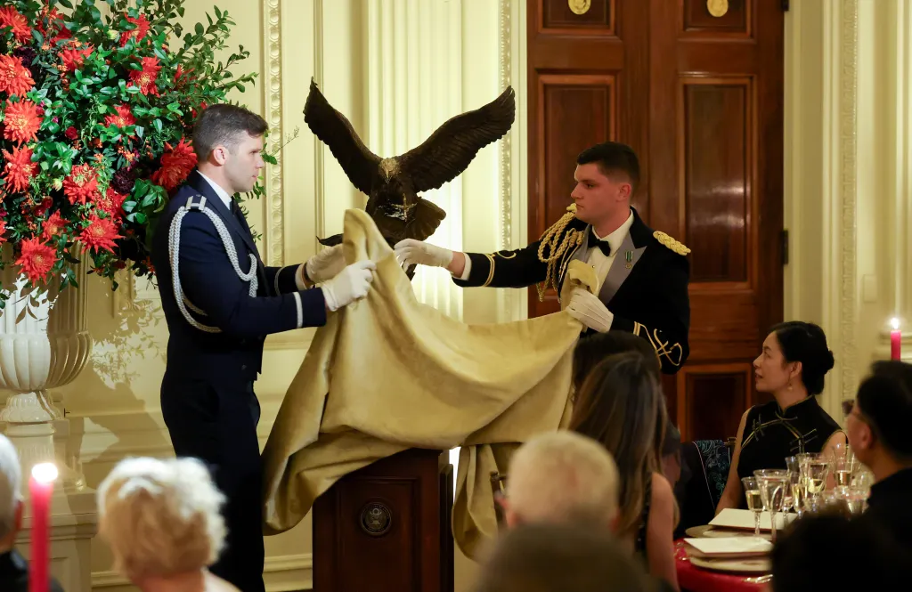 Two men in military dress uniforms unveil a bald eagle statue as a gift for Chinese President Xi Jinping.