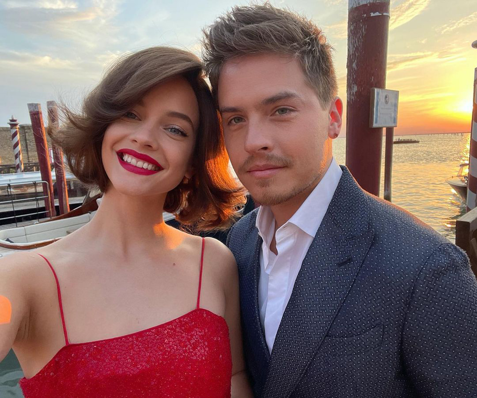 Barbara Palvin and Dylan Sprouse take a selfie with the sunset over the water in the background.