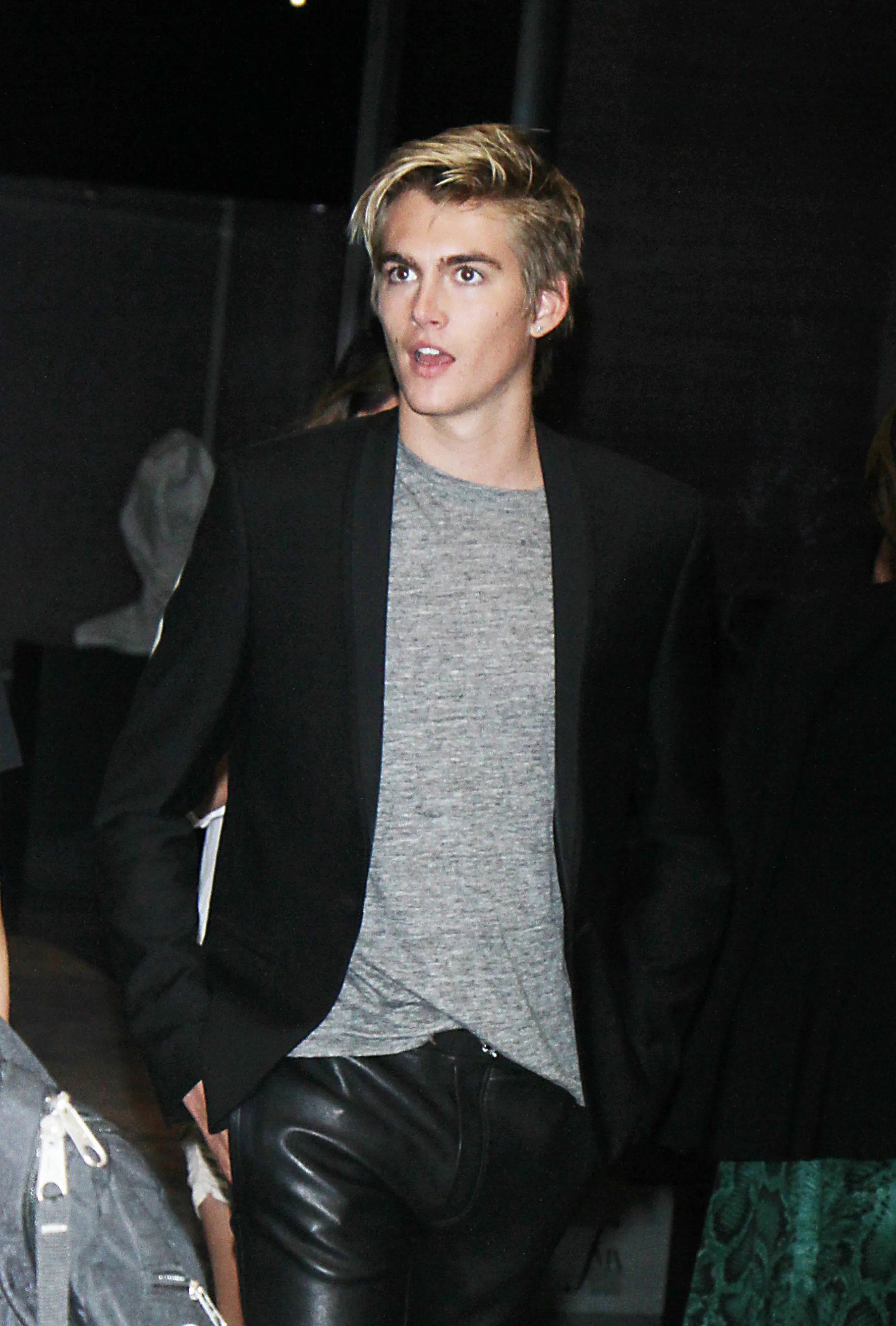 Presley Walker Gerber dressed in a black blazer, a gray t-shirt, and black leather pants.