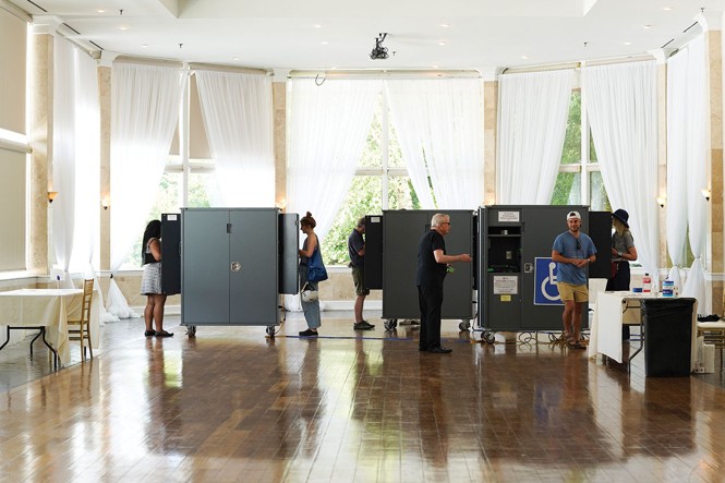 photo of high-ceilinged room with large windows and wood floors being used as voting center with booths and tables