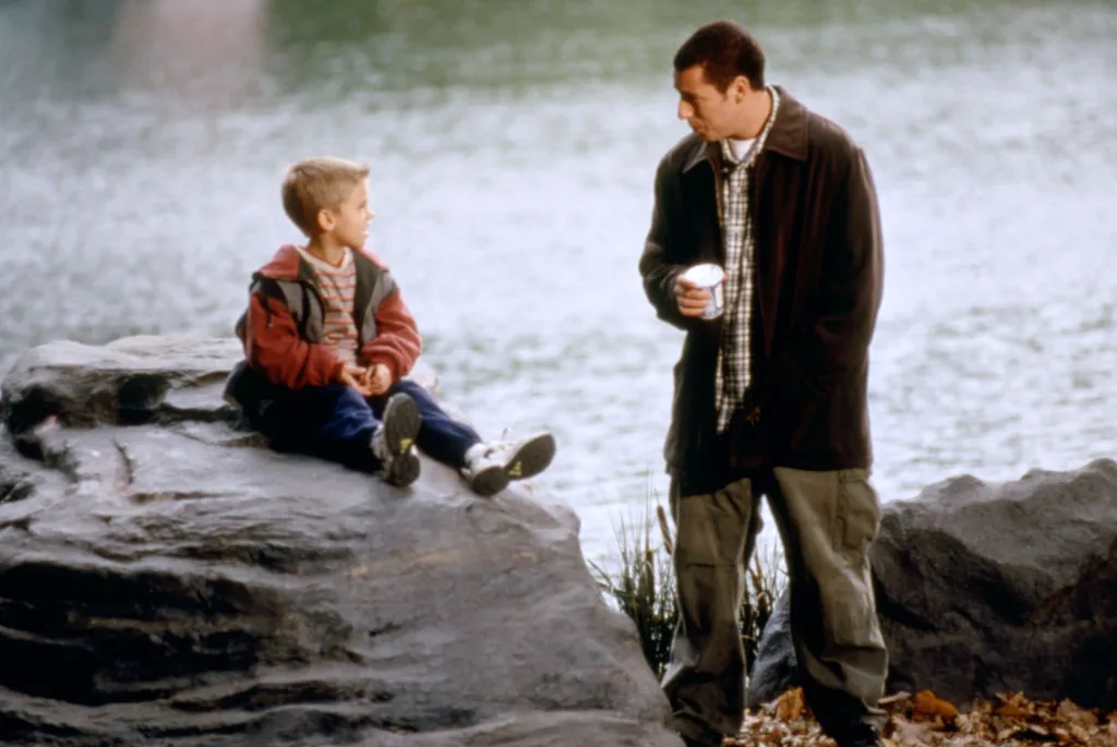 Adam Sandler and Cole Sprouse sitting by the water in 